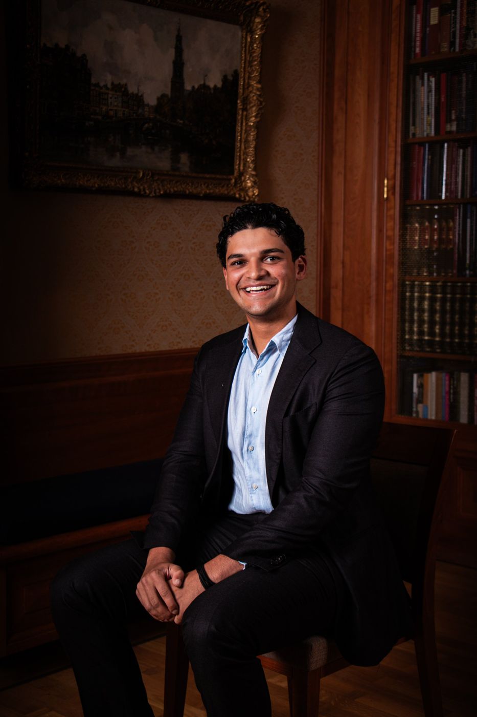 Lachende man in pak op een stoel in een klassieke bibliotheek